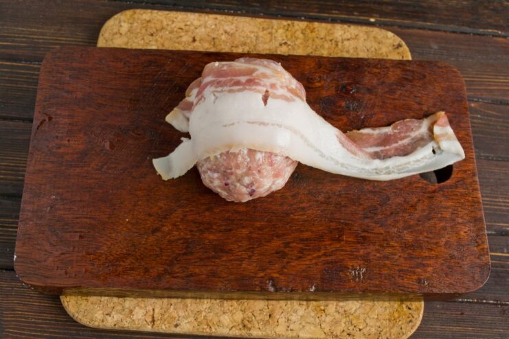 How to Wrap Stuffed Cutlets in Bacon A stuffed meat patty being carefully wrapped with thin slices of bacon.