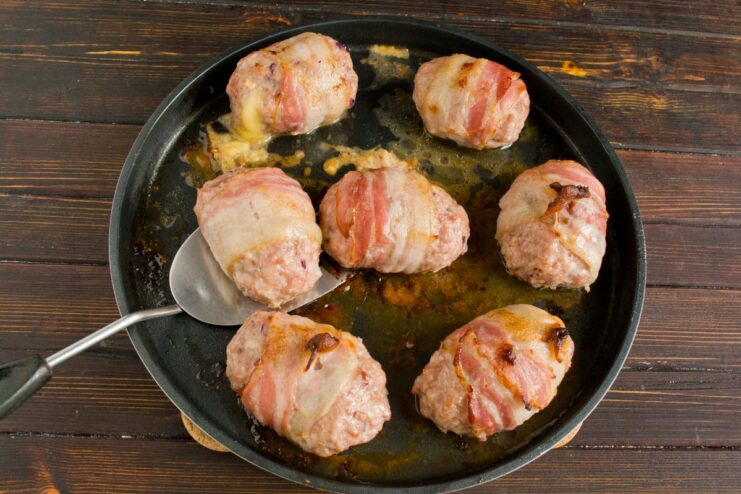 Baking the Cutlets to Golden-Brown Perfection Bacon-wrapped cutlets baking in a skillet inside an oven.