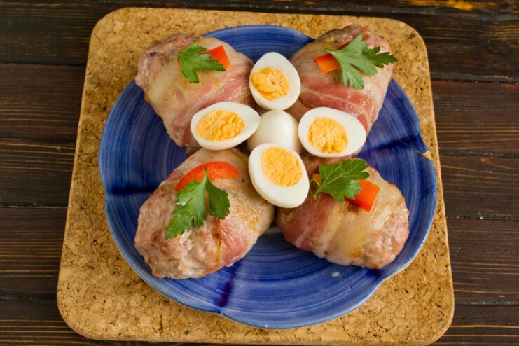 Delicious Bacon-Wrapped Cutlets with a Molten Cheese Center A plate of finished cheese-stuffed cutlets baked in bacon, garnished with herbs and quail eggs.