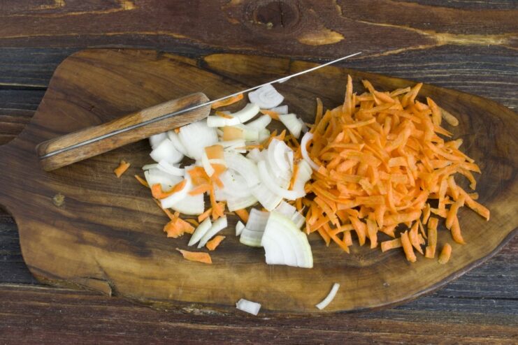 Sautéing vegetables to build a flavorful base Chopped onions and grated carrots being sautéed in a frying pan.