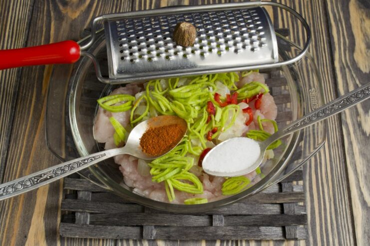 Seasoning the ground chicken with chopped chili, grated nutmeg, and salt.