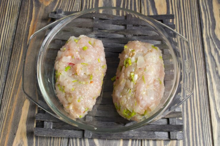 Two oblong-shaped raw chicken kotlety formed and ready for the next step.