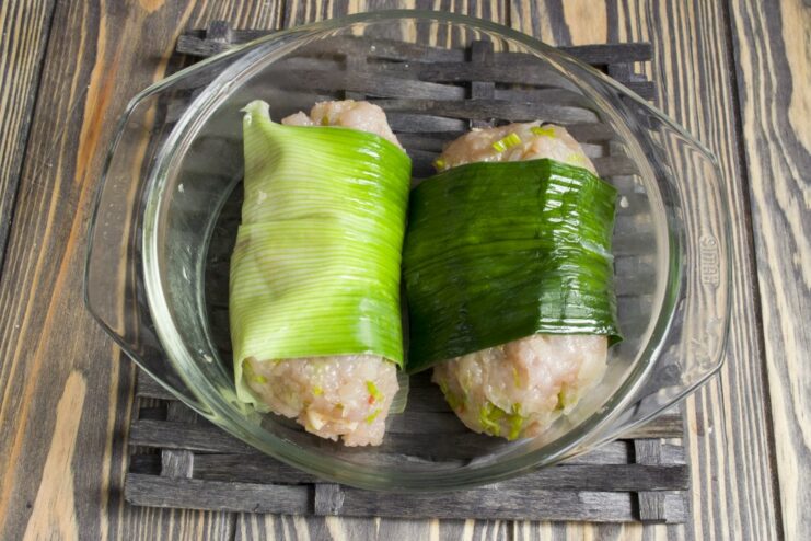 Chicken kotlety wrapped in blanched leek leaves, placed in a dish for microwaving.