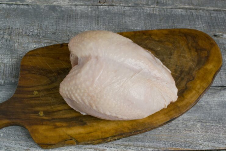 Properly preparing the chicken: washing the breast under cold water. A raw chicken breast being rinsed under a stream of cold water in a kitchen sink.