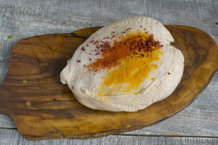 Drying and seasoning the chicken after its 24-hour brine. A brined chicken breast on a surface, being generously coated with various spices.