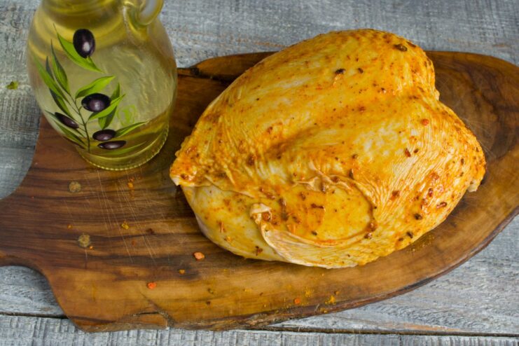 Massaging oil and spices into the chicken for an even flavor coating. Hands rubbing a mixture of olive oil and spices onto a raw chicken breast.