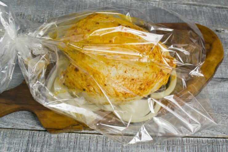 Creating a flavorful base of onions for the chicken in the roasting bag. A seasoned chicken breast being placed on a bed of thick onion rings inside a roasting bag.