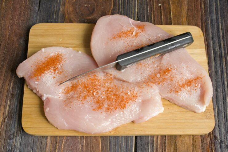 How to prepare chicken breast for steaming: seasoning with paprika and salt. Raw chicken breast fillet seasoned with paprika and salt on a cutting board.