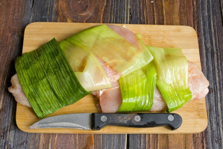 A simple trick for juicy chicken: wrapping it in leek leaves before steaming. Chicken breast wrapped in green leek leaves placed in a steamer basket.