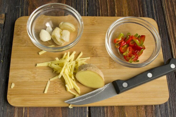 Building a flavor base: sautéing aromatics for the stewed cabbage. Chopped ginger, chili, and garlic being sautéed in a pan with oil.