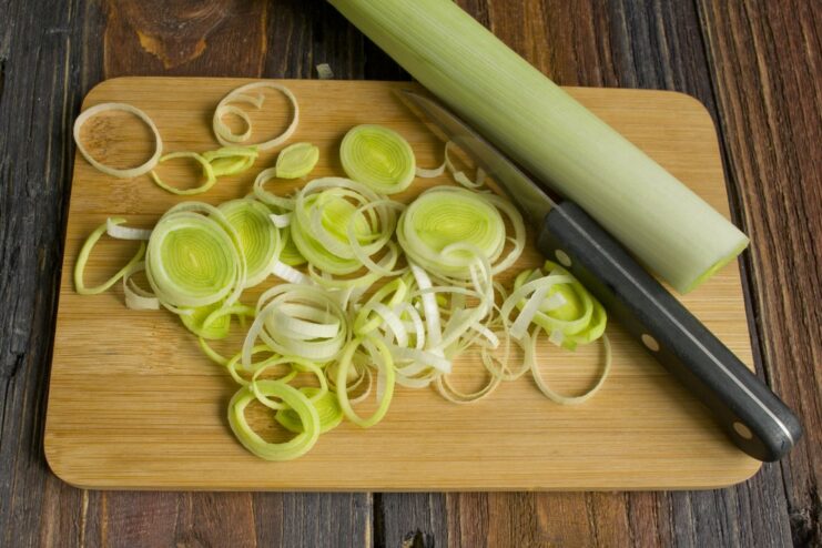 Adding sliced leek to the aromatic base for extra flavor. Sliced leek being added to the pan with sautéed ginger, chili, and garlic.