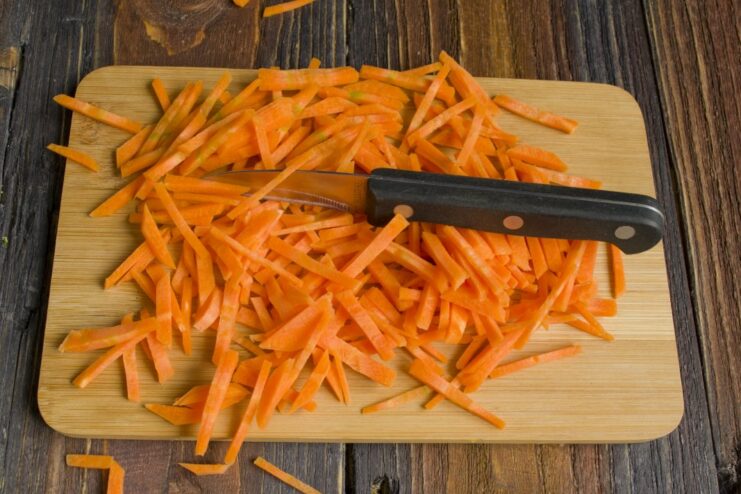 Adding sweetness and color with thinly sliced carrots. Thinly sliced carrots being added to the vegetables in the pan.