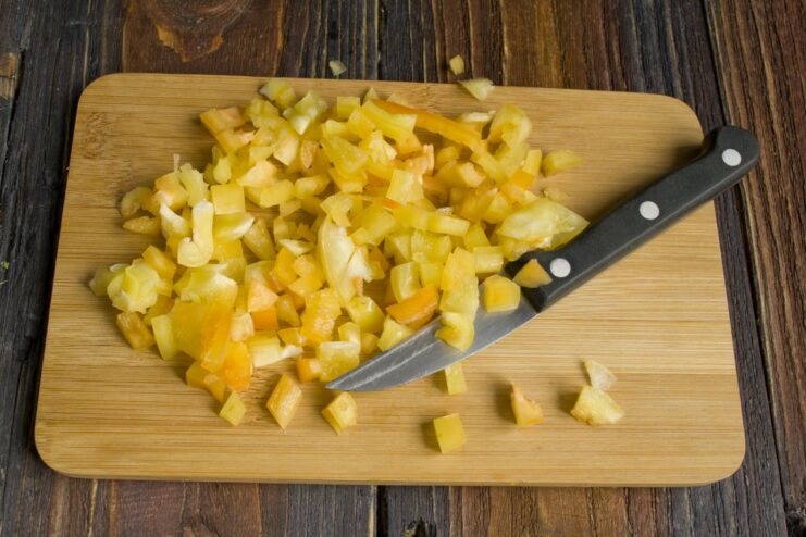 Enhancing the vegetable side with diced sweet bell pepper. Diced bell pepper being added to the pan with other vegetables.