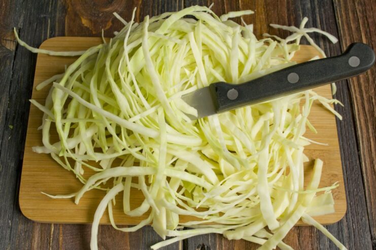 The main ingredient for the side dish: adding shredded cabbage. Shredded white cabbage being added to the pan of sautéed vegetables.