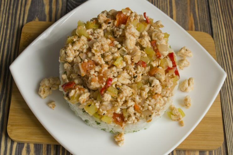 Assembling the dish: a bed of rice topped with savory chicken A plate being assembled with a layer of rice and a topping of chicken and vegetables.