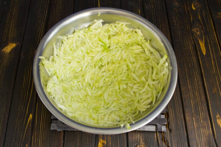 Preparing Zucchini: Grating and Salting to Remove Excess Water Close-up of freshly grated zucchini in a bowl, being mixed with salt.
