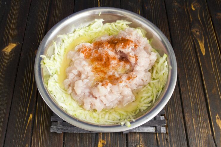 Seasoning the Chicken Cutlet Mixture with Sweet Paprika Sprinkling ground sweet paprika over the chicken and zucchini mixture in a bowl.