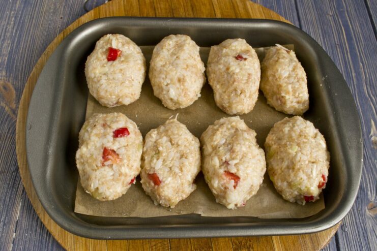 Shaping the Tefteli and Arranging them for Baking Raw oval-shaped chicken tefteli arranged on a parchment-lined baking sheet.