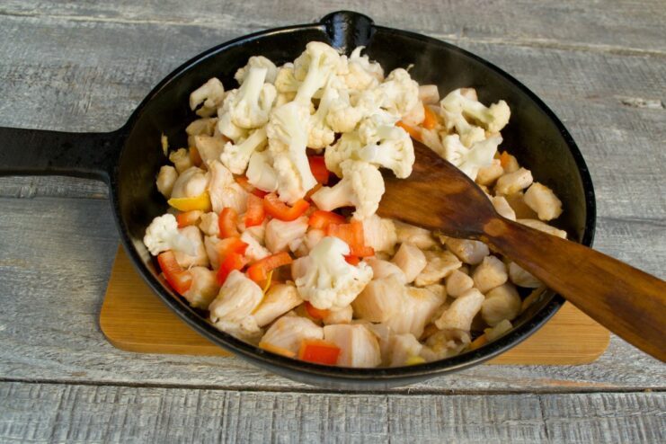 Incorporating Cauliflower for Extra Crunch Blanched cauliflower florets being added to the chicken and vegetable stir-fry in the skillet.