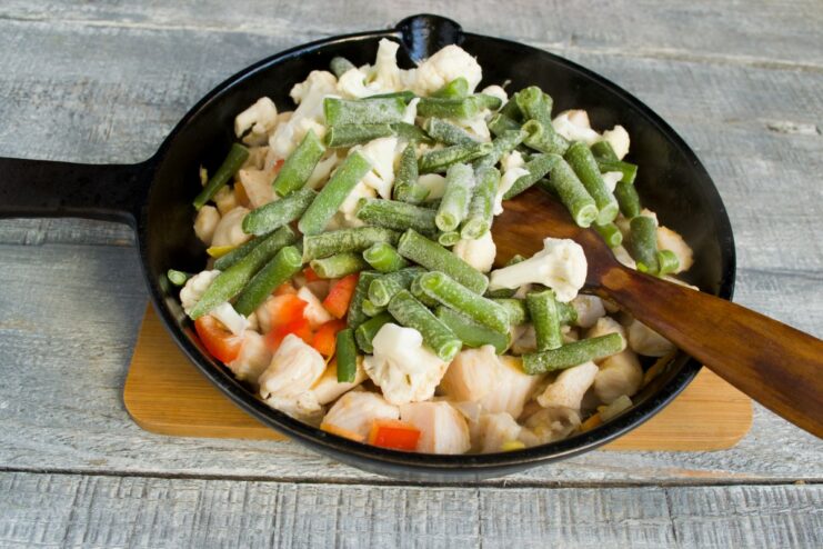 Adding Green Beans to the Stir-Fry Frozen or fresh green beans being added to the skillet with the Chinese-style chicken and vegetables.