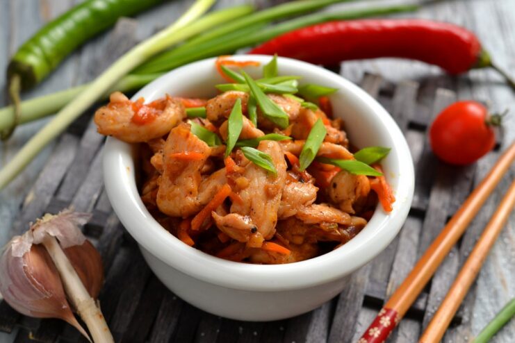 A white bowl filled with sweet and sour chicken, garnished with fresh green onions.