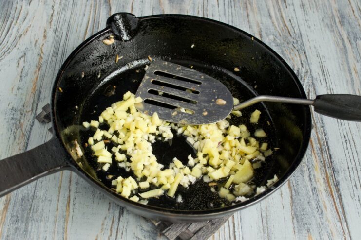 Building the Aromatic Base with Ginger and Garlic Minced ginger and garlic being sautéed in a hot pan with oil.