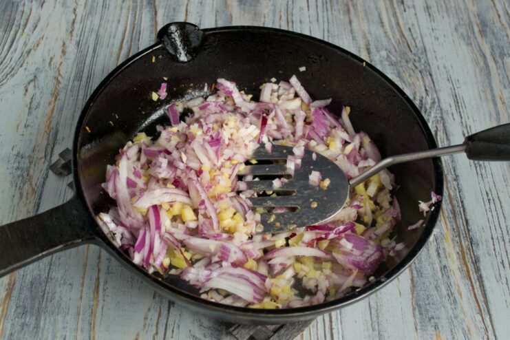 Sautéing Red Onion Until Soft and Translucent Chopped red onion being added to the sautéed ginger and garlic in a pan.