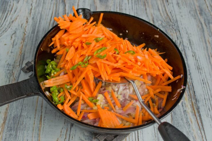 Cooking the Vegetables Until Crisp-Tender Shredded carrots and chopped green bell pepper being stir-fried in a pan with onions.