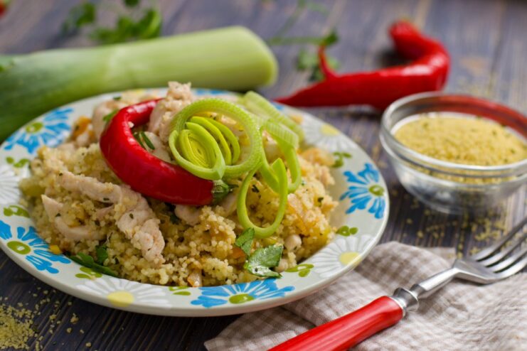 A plate of ready-to-eat couscous with chicken and fresh vegetables, garnished with herbs.
