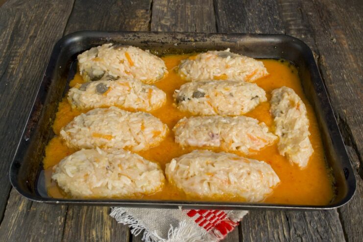 Step 6: Form the rolls and place them in the sauce-filled baking dish Raw lazy cabbage rolls arranged in a white baking dish filled with tomato sauce.
