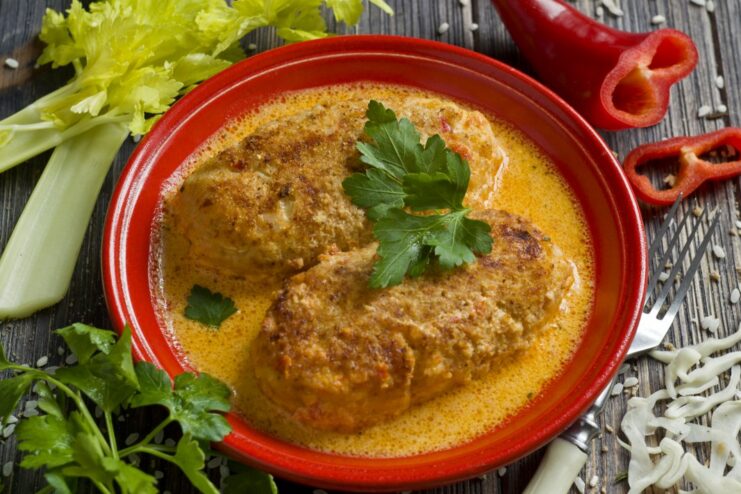 A plate of baked lazy cabbage rolls with rice and chicken in a creamy tomato sauce, garnished with fresh herbs.
