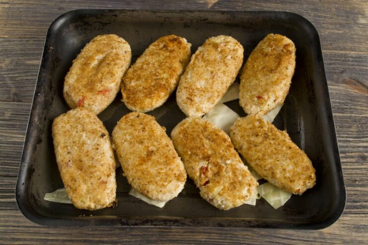 Arranging the Pan-Seared Rolls for Baking Golden-brown pan-fried lazy cabbage rolls arranged in a baking dish on top of cabbage leaves.