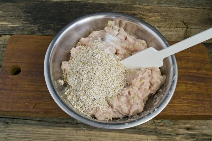 Combining all ingredients for the meat patties in a food processor. Ground meat mixture with vegetables, oat bran, and milk in a food processor bowl.