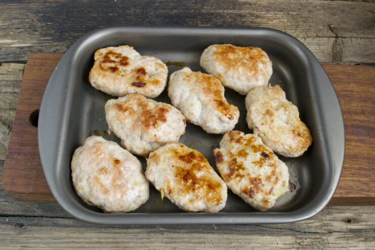 Baking the patties until golden brown and cooked through. Golden-brown meat patties baking on a sheet in the oven.