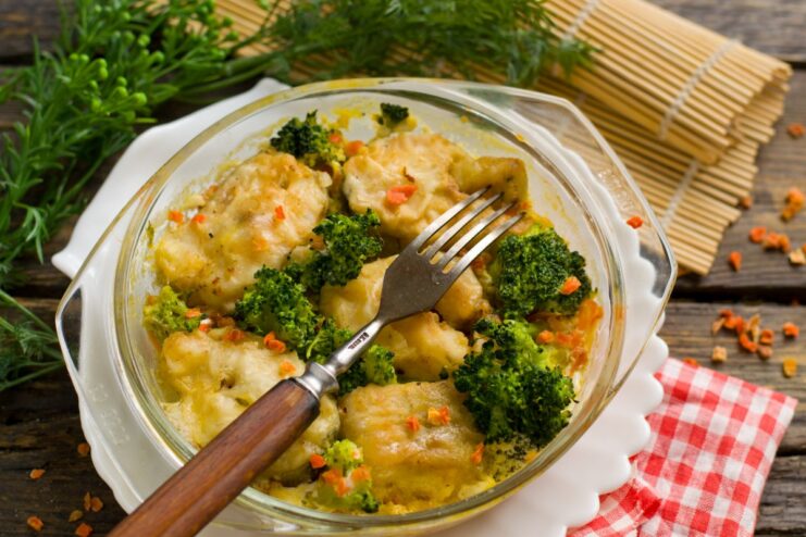 A serving of delicious baked pollock with vegetables in a white baking dish, garnished with fresh herbs.