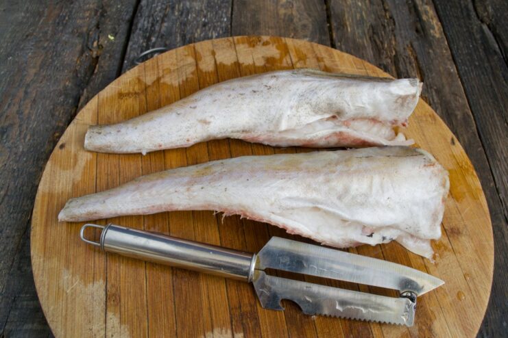 Patting Cleaned Pollock Dry with Paper Towels for a Crispier Skin Cleaned pollock fish being patted dry with a paper towel on a cutting board.