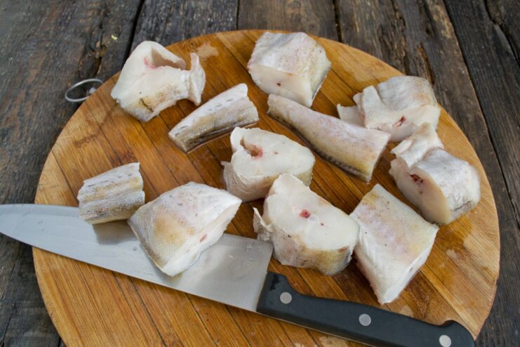 Seasoning Pollock Pieces with Salt and Pepper Before Cooking Pieces of raw pollock on a cutting board, seasoned with salt and pepper.