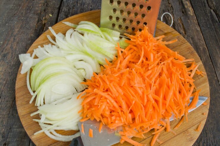 Preparing the Vegetable Base: Sliced Onions and Grated Carrots A pile of grated carrots and thinly sliced yellow onions on a cutting board.