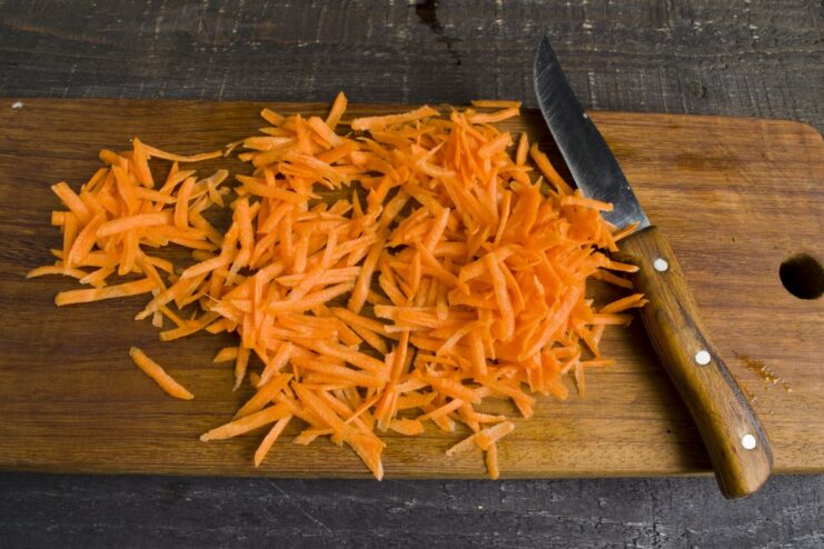 Grating Carrots for a Sweet and Flavorful Sauce Fresh carrots being grated on a box grater.