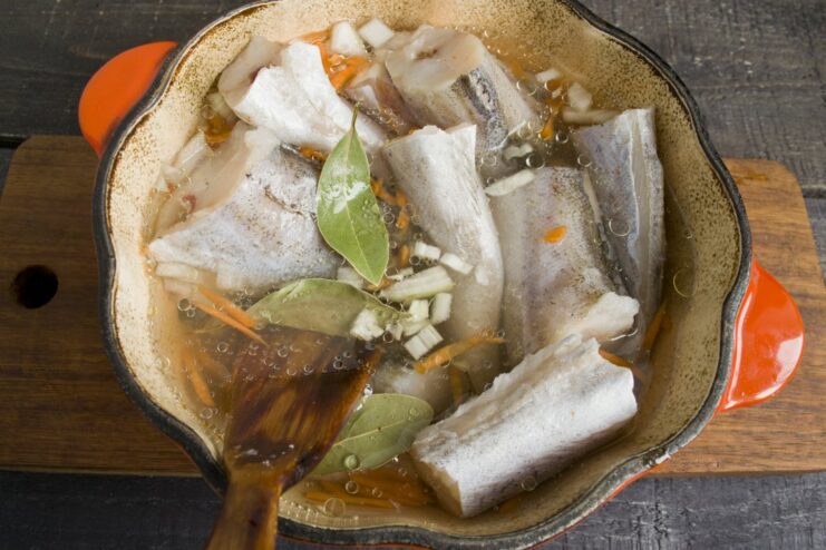 Layering Ingredients for Polish-Style Pollock A pot layered with butter, onions, carrots, pollock pieces, and spices, covered with water.