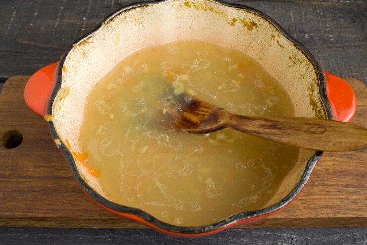 Creating a Smooth and Velvety Sauce Base An immersion blender pureeing the cooked vegetables and broth in a pot to create a smooth sauce.