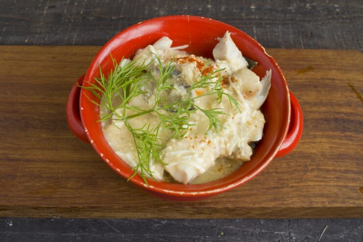 Serving the Pollock: Topped with Sauce and Garnishes Deboned pollock in a bowl, being covered with hot Polish-style sauce and garnished with paprika.