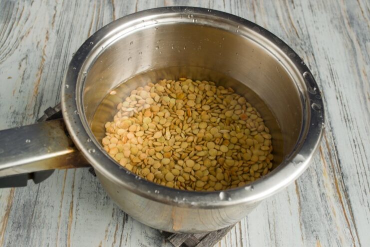 Cooking green lentils in a saucepan for the Mujadara recipe Green lentils being boiled in a saucepan on a stove.