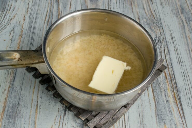 Cooking fluffy white rice in a separate pot White rice cooking in a pot with a piece of butter on top.