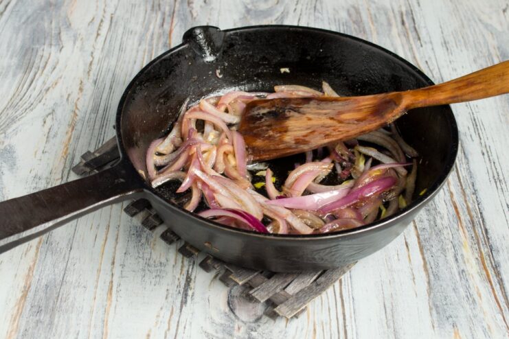 Sautéing sliced red onions until golden and caramelized Sliced red onions being fried in a pan until golden brown.