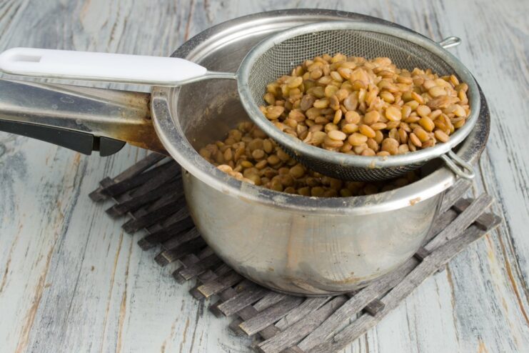Straining the cooked lentils to remove excess water Cooked green lentils being drained in a metal sieve.