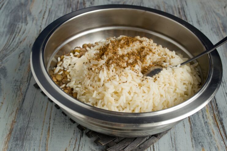 Sprinkling freshly ground spices over the rice and lentils Ground spices being added to the bowl of rice and lentils.