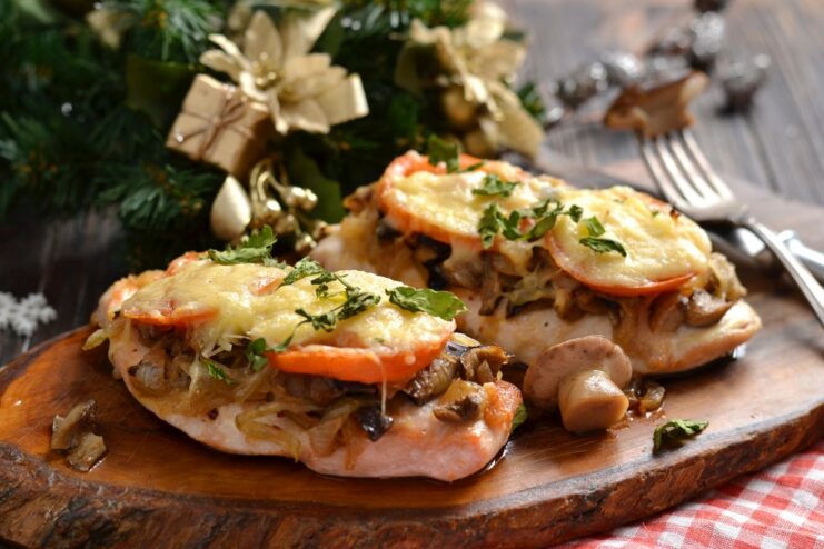 A plate of ready-to-eat chicken breast cutlets topped with melted cheese and tomatoes, garnished with herbs.