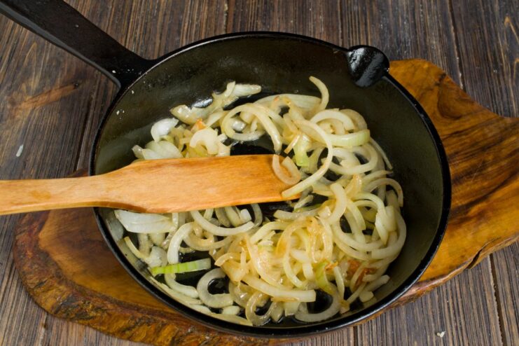 Sliced onions being sautéed in a pan until golden brown.