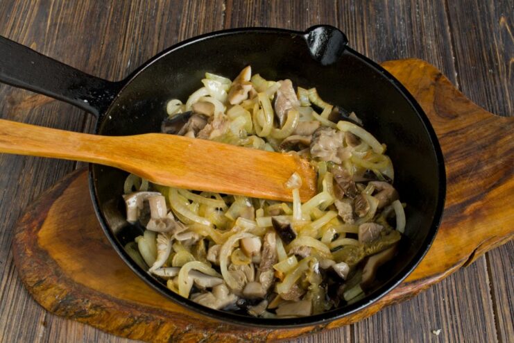 Chopped mushrooms being added to the pan with sautéed onions.